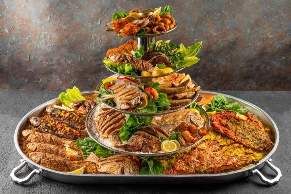 A generous multi tier platter filled with grilled fish, prawns, and spiced rice, made for group meals and special gatherings.